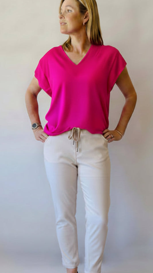 Woman wearing a neon pink V-neck top and white draw string pants 
